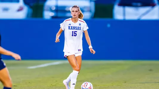 A soccer player wearing a Kansas jersey with the number 15 controls the ball on a field during a game.