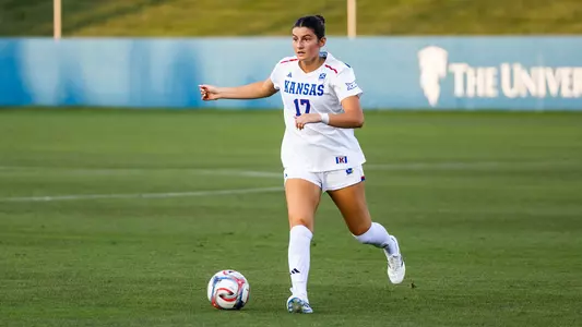 A soccer player in a white Kansas uniform with the number 17 controls the ball on a green field during a game.