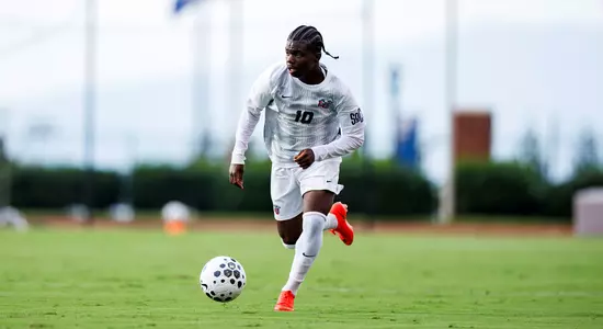 A soccer player in a white uniform with the number 10 runs across a green field, controlling a black and white ball.