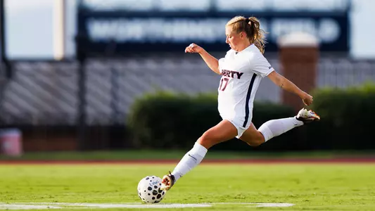 A soccer player in a white uniform with the number 17 kicks a ball on a green field during a game.